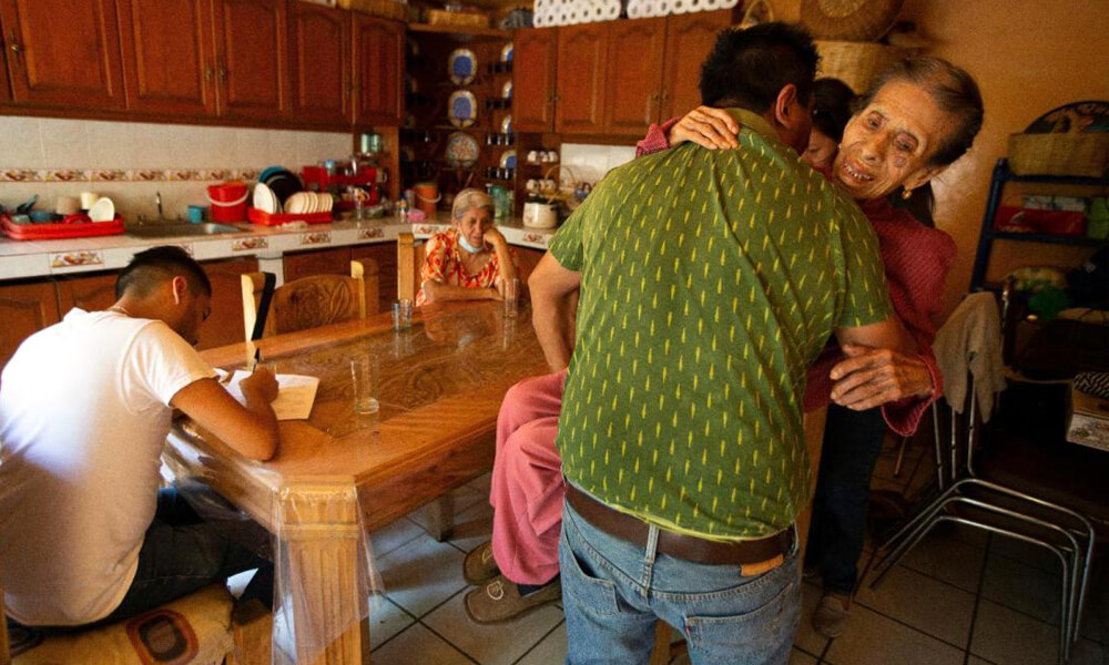 Orlando Infante lleva a su madre Beatriz Infante, una sobreviviente de COVID-19, a una silla de ruedas después de una visita médica de seguimiento del doctor Juan Antonio Salas, sentado a la izquierda, en su casa en la Ciudad de México, el viernes 5 de junio de 2020.